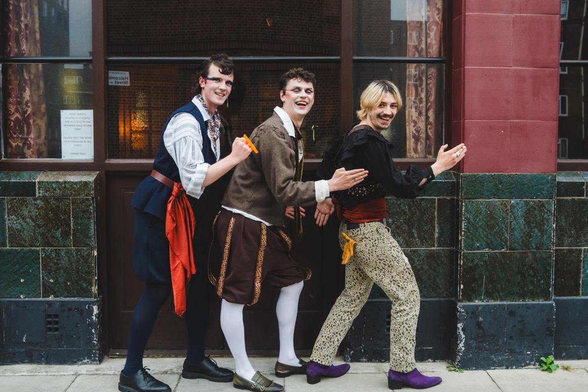 Candide in Tudor costume and white face paint, posing in a line outside a pub